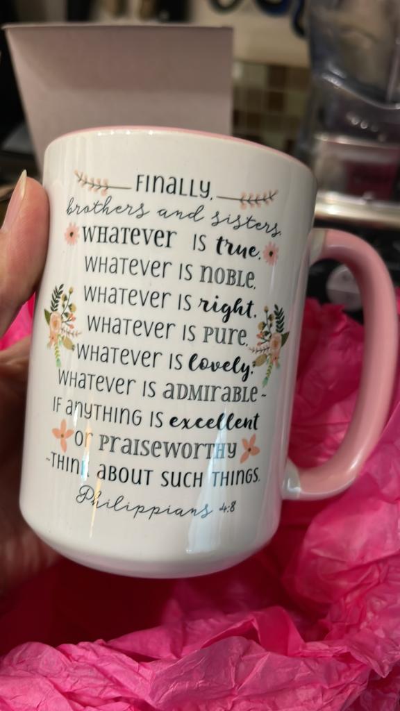 woman's hand holding white and pink floral coffee mug with Philippians 4:8 verse on it