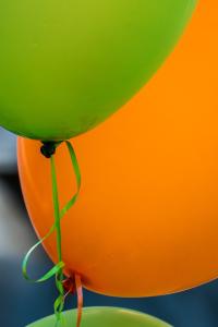 Close up of a green and an orange helium balloon at a party