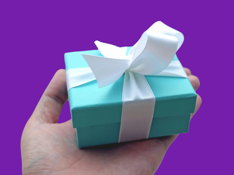 Blue Tiffany box with white satin ribbon, in man's hand, on purple background