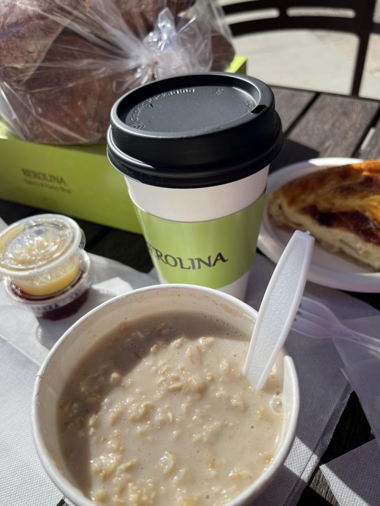 Oatmeal, latte in to-go cup, and slice of quiche from Berolina Bakery on an outdoor table