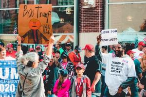 People protesting, a woman and a man holding different political signs