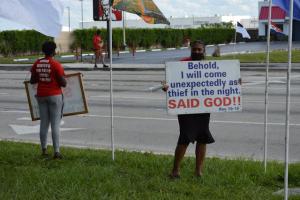 Two people standing with signs on a roadside with bible verses on them