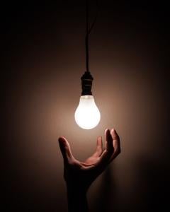 A hand reaching up to a lit lightbulb