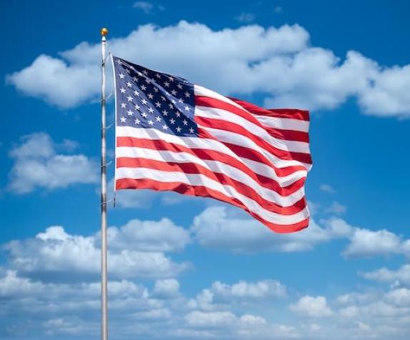 An American flag flies against a background of a blue sky with clouds.