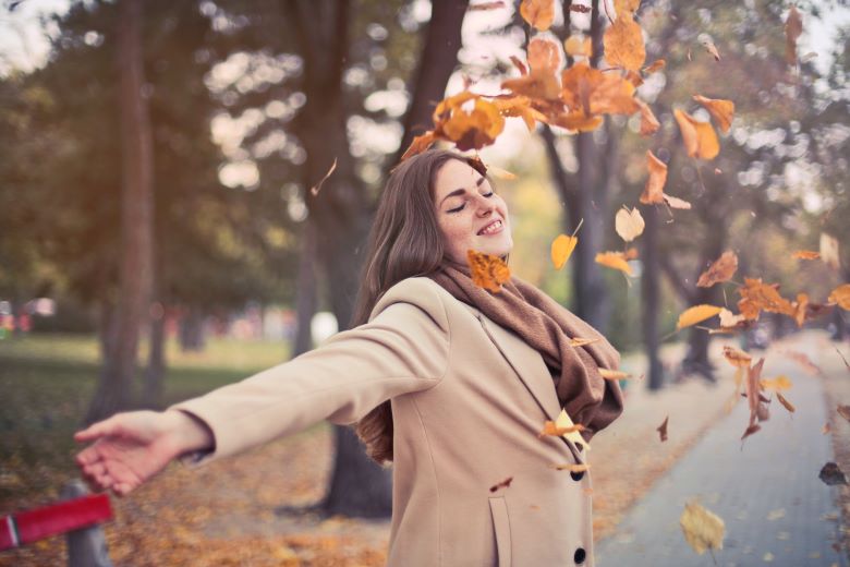 Woman Enjoys the Autumn Leaves Falling in a City Park