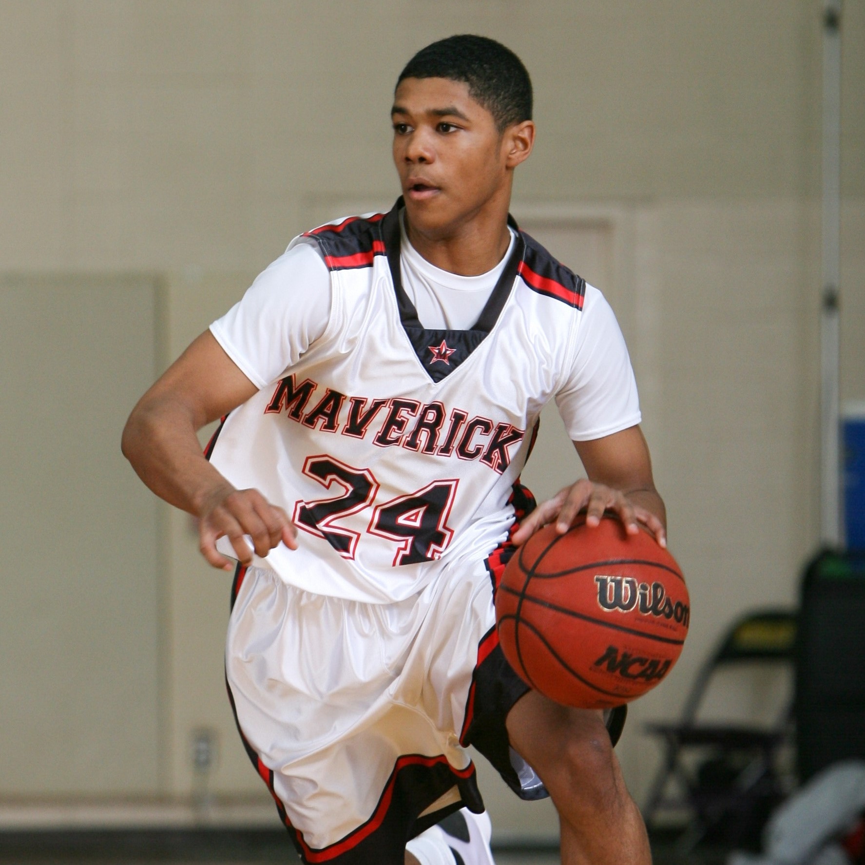 A male basketball player dribbles the basketball up the court.