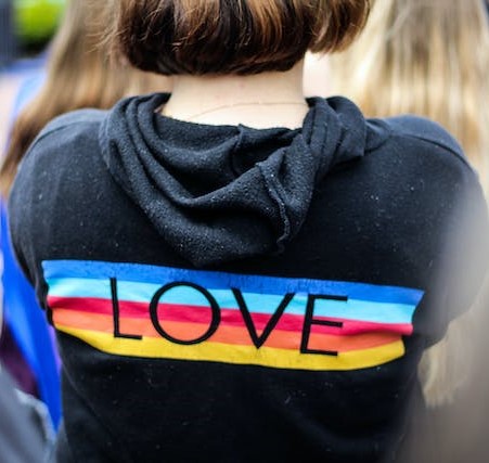 A teen girl wears a hoody with the word "love" laid over rainbow colors.