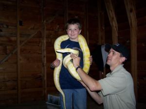 Boy holding a giant albino python around his neck. Assisted by a park ranger.