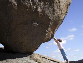 Person appearing to hold a giant boulder from rolling down hill.