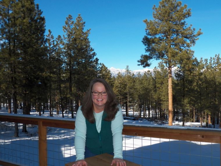 Woman standing on deck with snow-capped mountains in the background. 