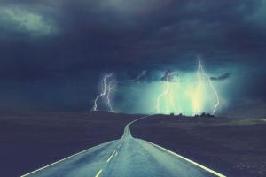 Paved road leading to a lightning storm and knowing we are not alone