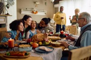 Happy multiracial parents and their kids laughing during family meal on Thanksgiving in dining room