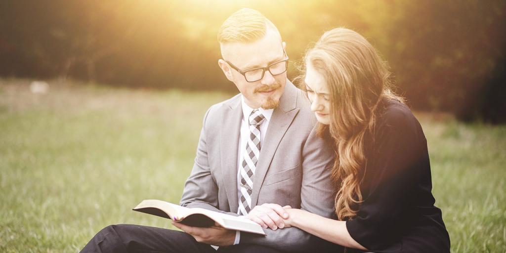 Man and woman sitting in the grass reading a Bible