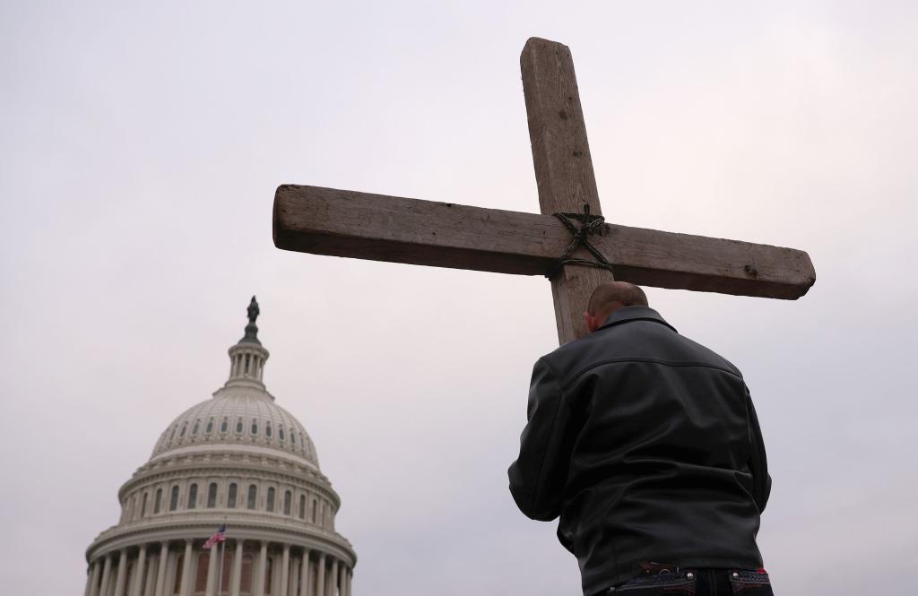 Man with wooden cross facing Capitol Hill and praying for America