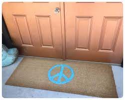 A front door mat on the ground by doors with a peace sign. 
