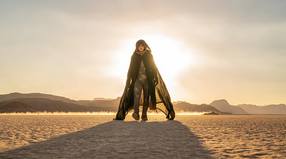 A man walks the desert alone as the sun sets