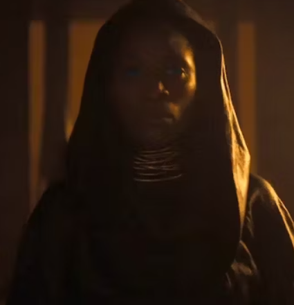 a woman in a hooded tunic in a dark room