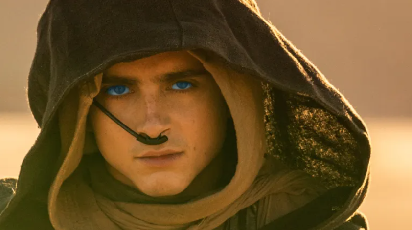 A man under a hood with blue eyes in a desert