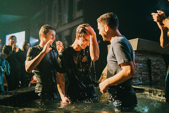 A young man getting baptized with two other pastors