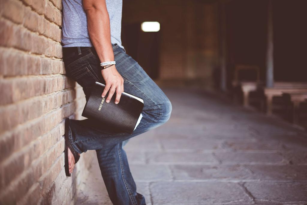 Young man leaning against wall holding a bible 