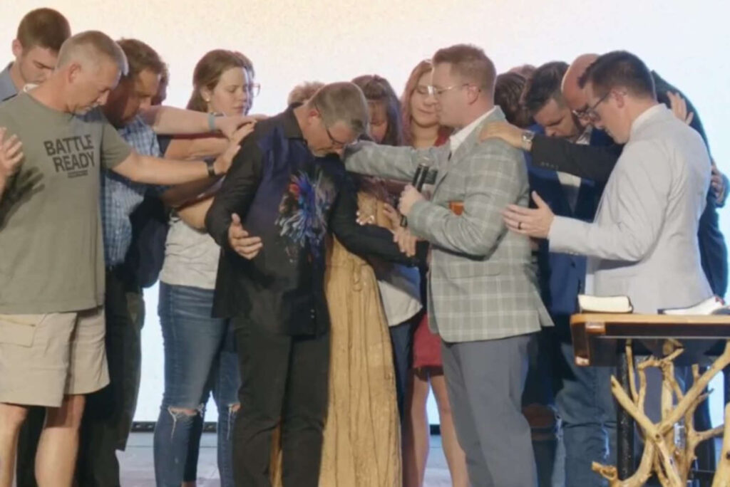 Group of people laying hands on a man who is receiving prayer