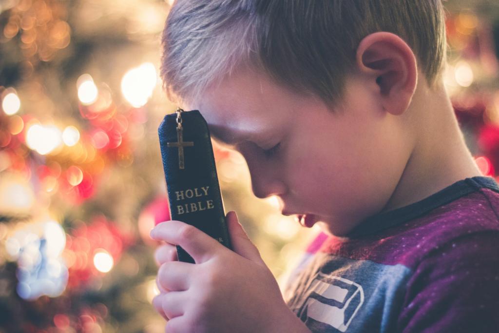 Little boy with his eyes closed placing the Bible up to his forehead