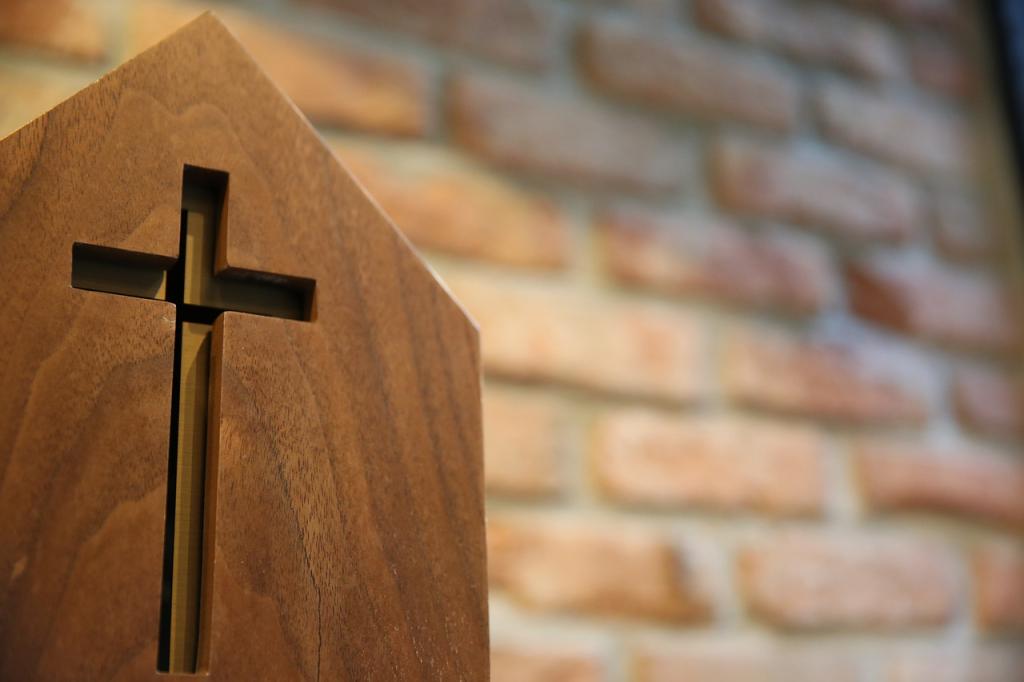 An engraved cross on a pew in front of a brick wall to discuss American religion