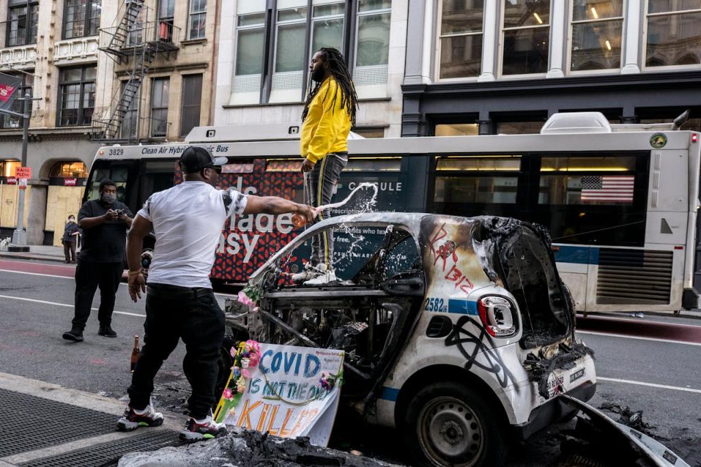 Protestor standing on top of a burned and vandalized car because of political authority
