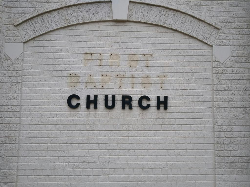 Letters spelling "Church" on a building wall with the letters spelling "First Baptist" are removed.