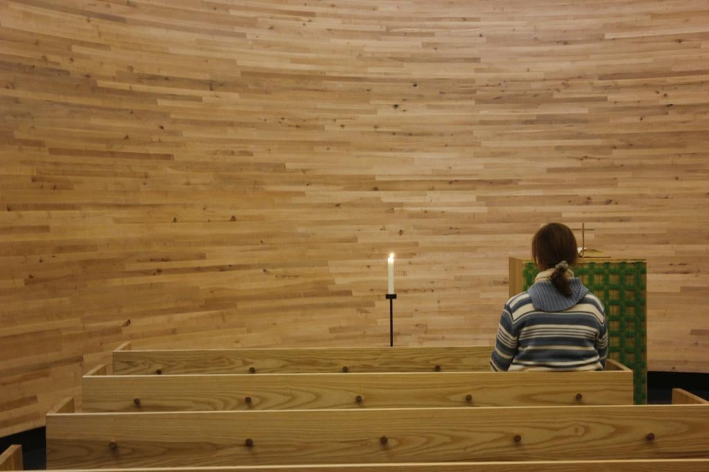 A young lady sitting in an empty chapel made of wood