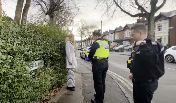 A woman standing on a curb being approached by two police officers
