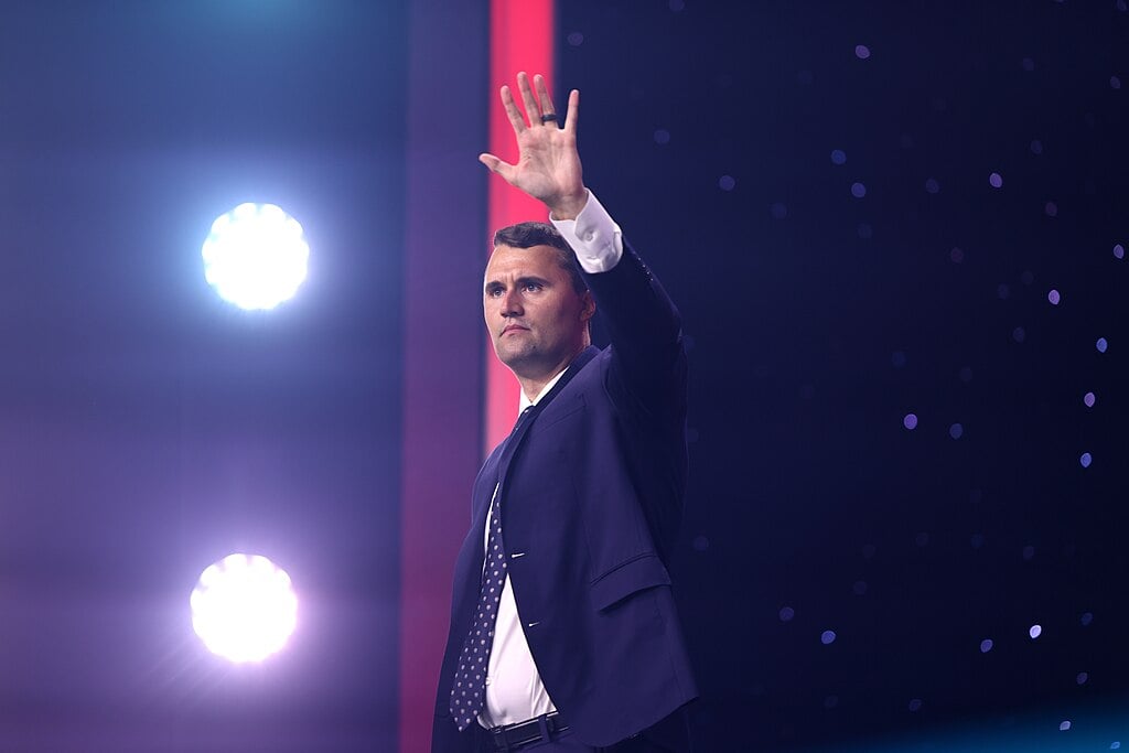 A man named Charlie Kirk waving to a large crowd on stage.