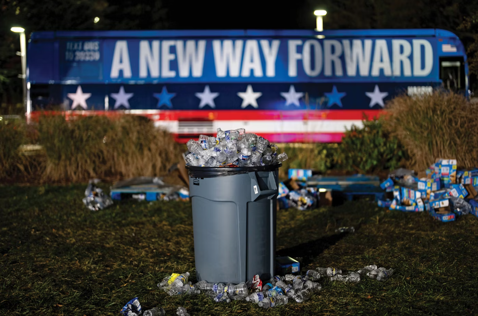 A banner on a bus reding "New Way Forward" behind a bin overflowing with trash, a message for both the DNC and GOP.