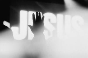 A raised hand among smoke in front of a JESUS banner