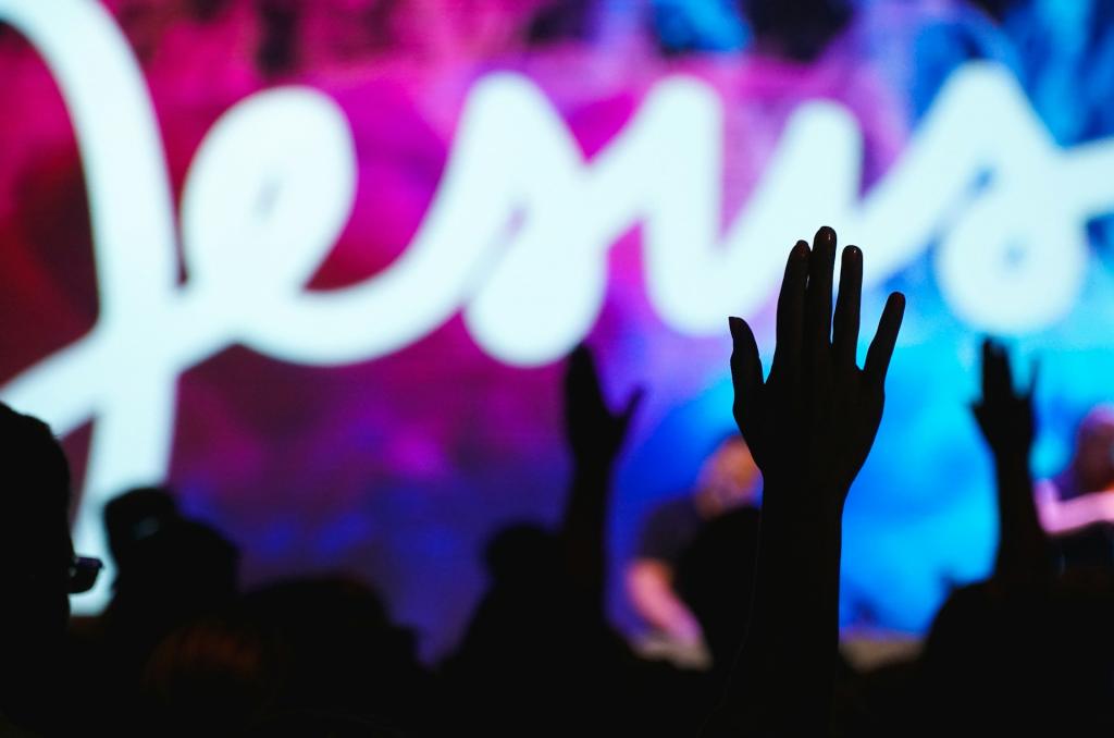Hand raised in praise of Jesus in front of neon Jesus sign.
