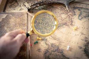 An older map being invesitgated by someone with a magnifying glass.