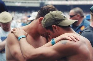 Two men, one with a backward baseball cap, praying for each other inside a football stadium