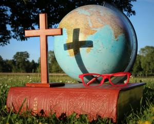 A cross, globe and a pair of red glasses on top of a Bible in a park symbolizing a Biblical Worldview