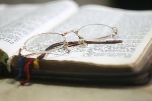 A Bible opened among several bookmarks and a pair of glasses on top of it.
