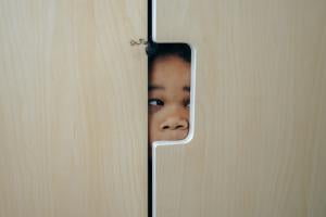 A young black girl peering through a hole in a closet door