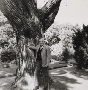 A black and white image of JRR Tolkien posing by his favorite tree on Oxford's campus