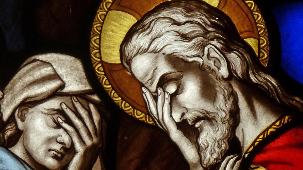 A stained glass window panel of a church showing Jesus in deep thought, holding his head in his hand.