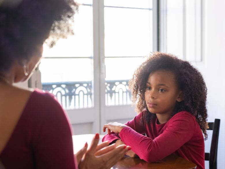 Young African American girl sitting at a table with her mother.