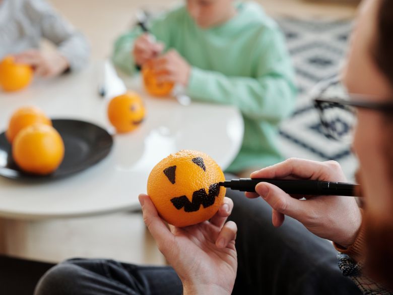 A family decorating oranges as jackolanterns for Halloween.