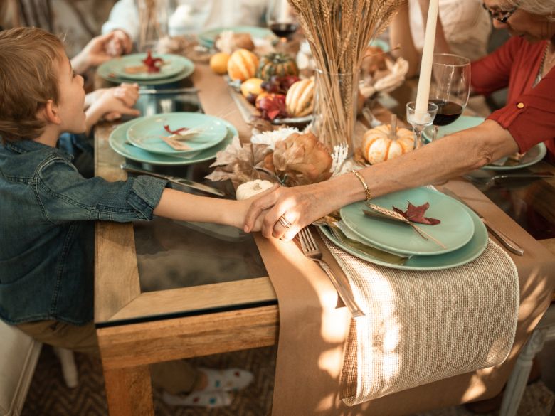 family with little boy holding hands around the table and praying at thanksgiving dinner