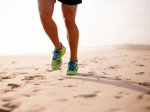 Picture of the legs of a runner running on the beach in the footsteps of others before him