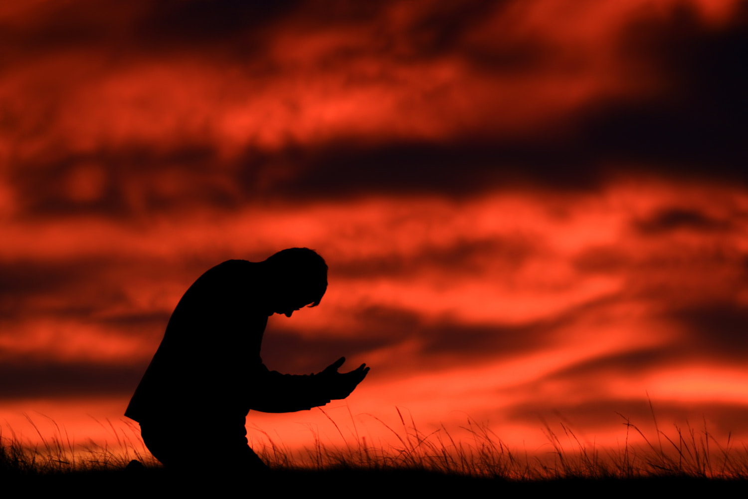 Someone on their knees praying against a red sky