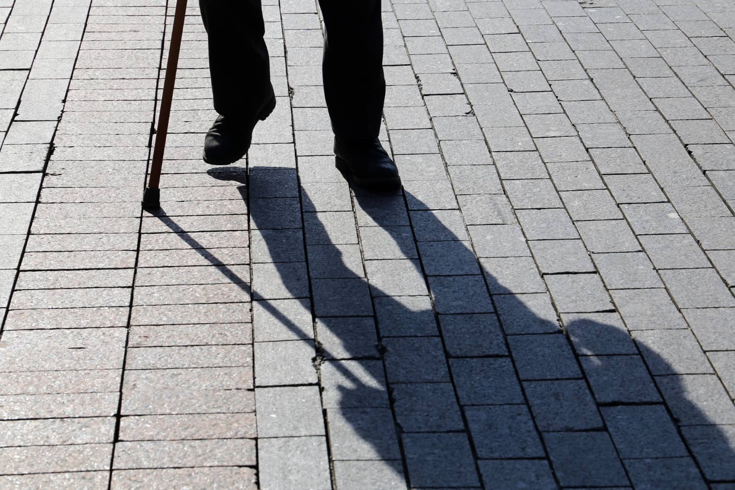 The shadow of an old man with a walking stick on the pavements