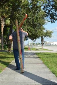Man carrying large cross down the sidewalk in a modern setting.
