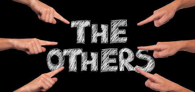 Black background with fingers pointing to words "The Others" appearing to be written in chalk